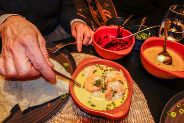 An assortment of Sri Lankan food in a Sri Lankan restaurant and a person taking shrimp in green curry sauce.