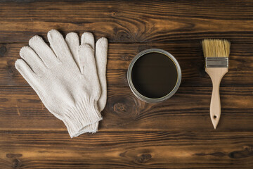 Brush, gloves and jar with a protective coating for wood on a wooden background.