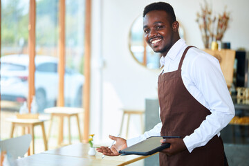 A black waiter or small restaurant operator invites customers to sit at the dining table.