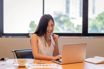 Tuinposter Asian businesswoman in casual suit are glad when completed doing online shopping via smart mobile phone application or technology laptop in modern office, business and lifestyle concept © THANANIT