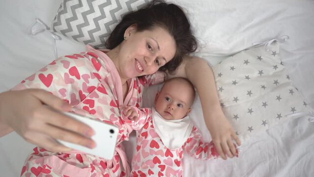 Mom takes a selfie with her newborn daughter while lying on the bed