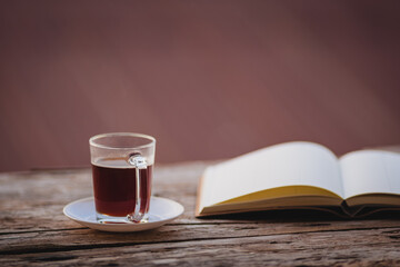 A cup of hot morning coffee on wooden table with a diary notebook at the balcony of the sleeping room to welcome sunshine in the morning, a glass of black coffee with a notebook on the wooden table