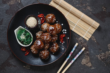 Black plate with roasted pork meatballs in teriyaki sauce, above view on a brown stone background, horizontal shot