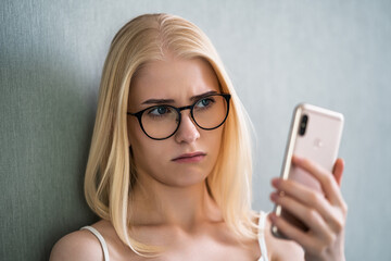 A girl with a phone in her hand sits with anxiety in her eyes