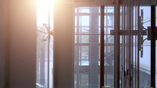 Moving elevator in modern commercial building. The elevator goes up. There is a flash of sunlight in the upper left corner. The mechanical structure inside the elevator.