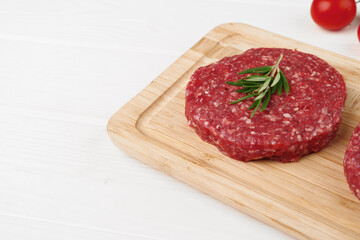 Two raw beef burger patties on wooden board