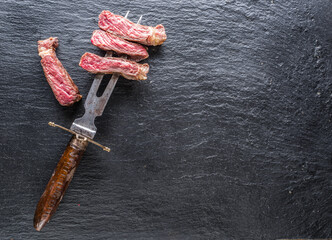 Rare medium cuts of ribeye steak on folk on gray cutting board. Top view.