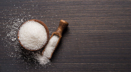 White refined sugar in wooden bowl and spoon on dark wooden table.