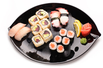 Black plate with different types of sushi on white background. Top view.