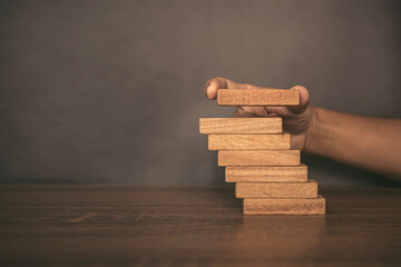 Close-up hand is placing wood block tower stacked in pyramid shape with caution to prevent collapse...
