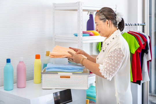 Happy Smiling Asian Senior Elderly Female Woman Folding Clothes Doing Laundry With Washing Machine, House Cleaning And Housekeeping Concept