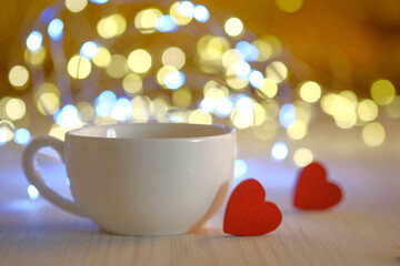 white cup and red hearts on a background of golden boke