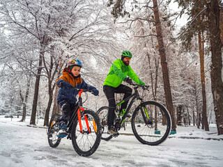 A father and his son ride a bikes in a winter park