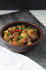 Stewed vegetables with spices in an earthen bowl on a dark gray slate or stone background. View from above.