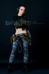 Fototapeta na wymiar Dressed in a black T-shirt, a curvy combat woman with short hair holds a rifle against a dark background.