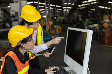 Two factory workers or technicians are using computer and technology to check stock in a heavy machinery warehouse