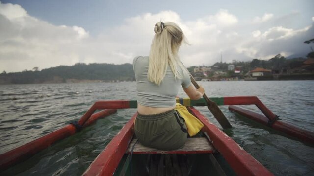 Blond Woman Rowing Outrigger With Oar In Bali