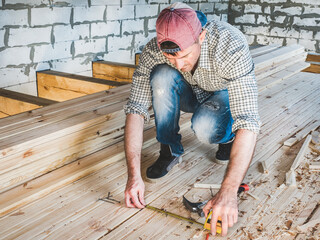 Stylish guy in a baseball cap, jeans and a shirt, working with tools on wood inside the house under construction. Concept of construction and repair	