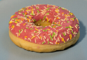 Pink doughnut or donut with colored sprinkles on a blue background. Bitten off American bagel.