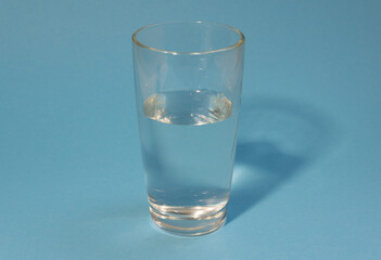 Half-filled glass of clean cold water on a light blue background. Healthy life, proper nutrition, drink plenty of water.