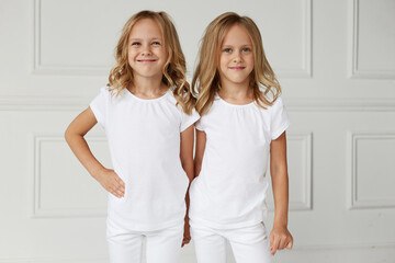 Two little smiling kids girls in white clothes isolated on white background. Twin girls they hold hands. Horizontal view.
