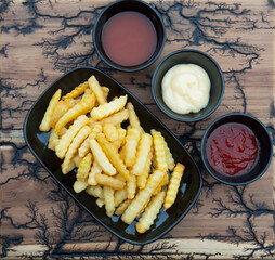 Top view of French fries with sauces on wood plate