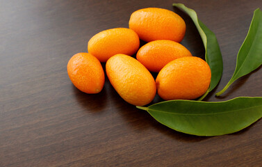 kumquat fruits on a wooden table, small citrus fruits and leaves