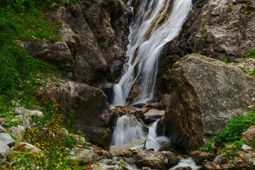 Naklejka na ściany i meble waterfall between rocks with flowers and plants on the side