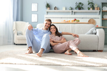 The happy couple in pajamas sitting on the floor background of the sofa in the living room.