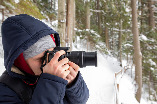 Man photographer with camera takes pictures of winter forest landscape.