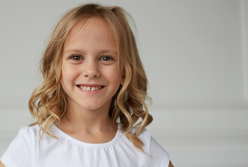 Portrait of a little girl smiling and looking at the camera, dressed in a white shirt, brave and pretty girl, on a white background.
