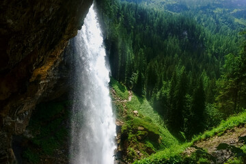 wonderful high waterfall over a cliff in the mountains with a forest