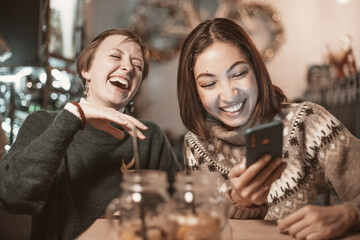 Two funny female friends look at new memes on social networks and laugh out loud in cafe. Smartphone with online Internet access - a new type of leisure for group of friends