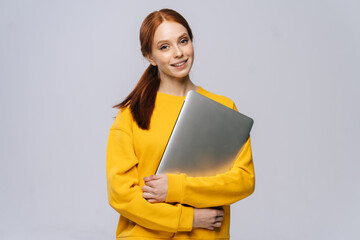 Cheerful young woman student holding closed laptop computer and looking at camera on isolated white...