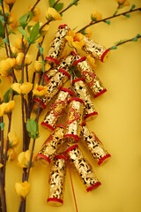 Golden firecrackers with best wishes inscription and blooming apricot branches on yellow table prepared for Tet Lunar New Year