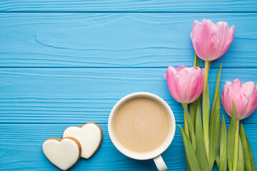 Fototapeta na wymiar Flatlay photo of three beautiful tulips cup of tasty beverage and white cookies in shape of hearts on bright color desk backdrop