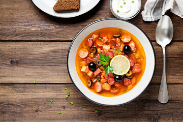Traditional Russian meat soup Solyanka in bowl on rustic wooden table. Top view. Copy space.