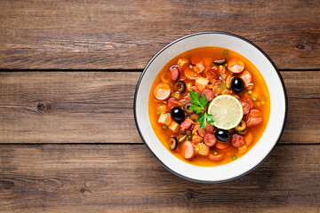 Traditional Russian meat soup Solyanka in bowl on rustic wooden table. Top view. Copy space.