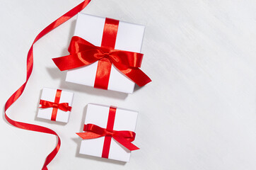 Gentle wedding set of white gift boxes with red bow on white wood board, copy space, top view.