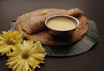 Puran Poli, also known as Holige, is an Indian sweet flatbread from India consumed mostly during Holi festival. Served on banana leaf with pure Ghee over black background.