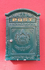 A green colored metal mail box on a red wall