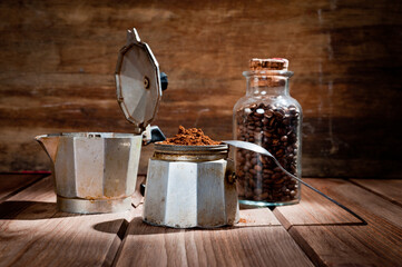 A geyser type metal coffee maker, photographed against a vintage wooden background with coffee beans.