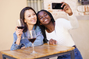 Two women making a selfie with a smartphone while having a glass of wine.