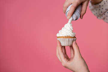 young charming female pastry chef decorates a muffin with whipped cream. pastry chef on a pink...