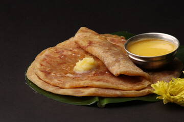 Puran Poli, also known as Holige, is an Indian sweet flatbread from India consumed mostly during Holi festival. Served on banana leaf with pure Ghee over black background.