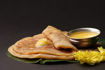 Puran Poli, also known as Holige, is an Indian sweet flatbread from India consumed mostly during Holi festival. Served on banana leaf with pure Ghee over black background. - obrazy, fototapety, plakaty