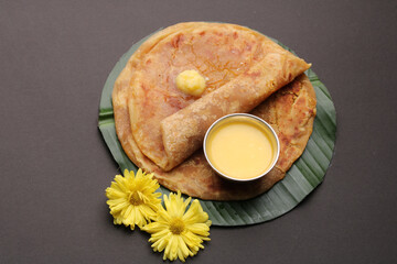 Puran Poli, also known as Holige, is an Indian sweet flatbread from India consumed mostly during Holi festival. Served on banana leaf with pure Ghee over black background.