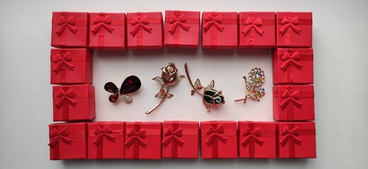 Frame, rectangle from red gift boxes with four brooches in the middle. Top view perspective.