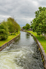 Middle River with water flowing towards Bridge Street amongst grass and trees with green foliage, Waterways of Galway, cloudy day in Galway City, Connacht Province, Ireland