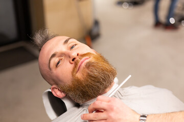 Obraz na płótnie Canvas European brutal man with a beard cut in a barbershop